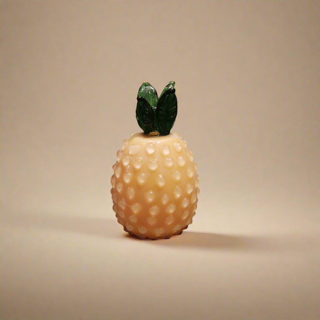 Handblown glass pineapple decoration with a yellow body and green leaves on top.