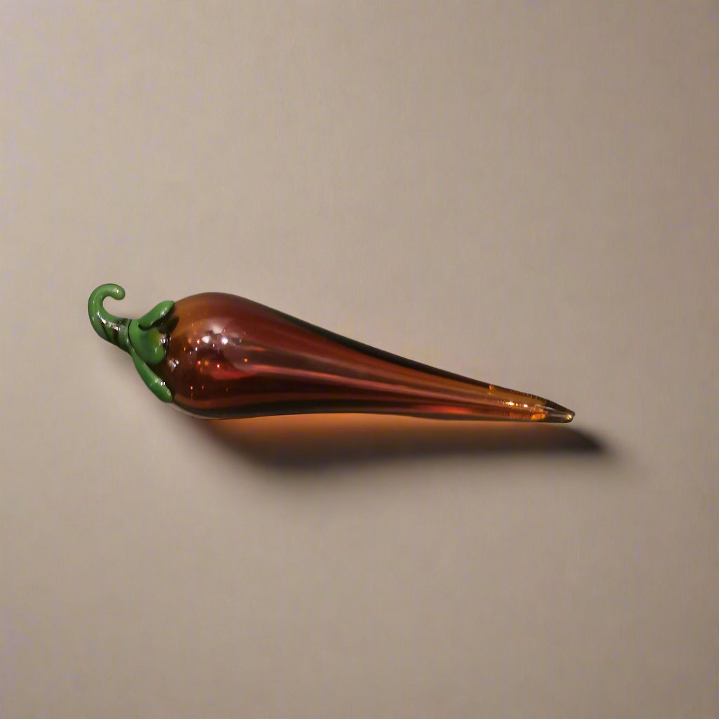 Handblown glass chilli decoration with a dark amber body and green stem.