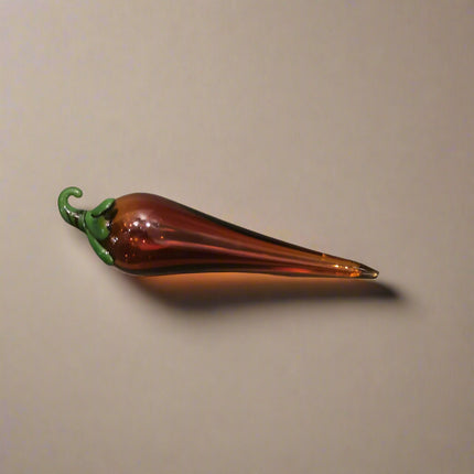 Handblown glass chilli decoration with a dark amber body and green stem.