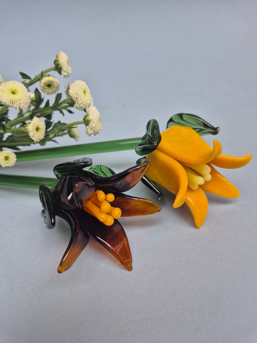 Two glass flowers, one yellow and one brown, on a gray background with small white flowers.
