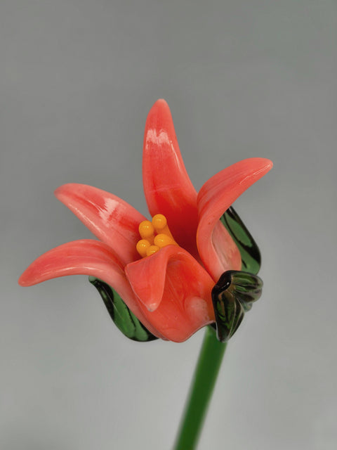 Glass flower sculpture with pink petals and yellow center on a gray background
