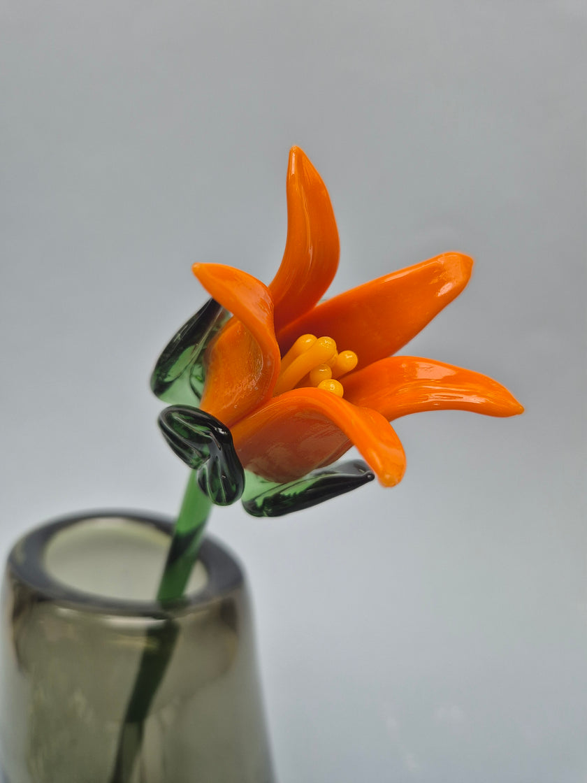 Glass flower sculpture of an orange lily on a gray background