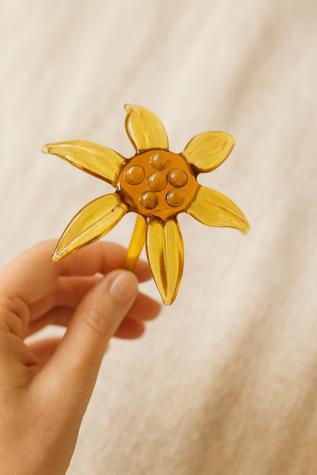 Hand holding a yellow sunflower-shaped object against a beige background