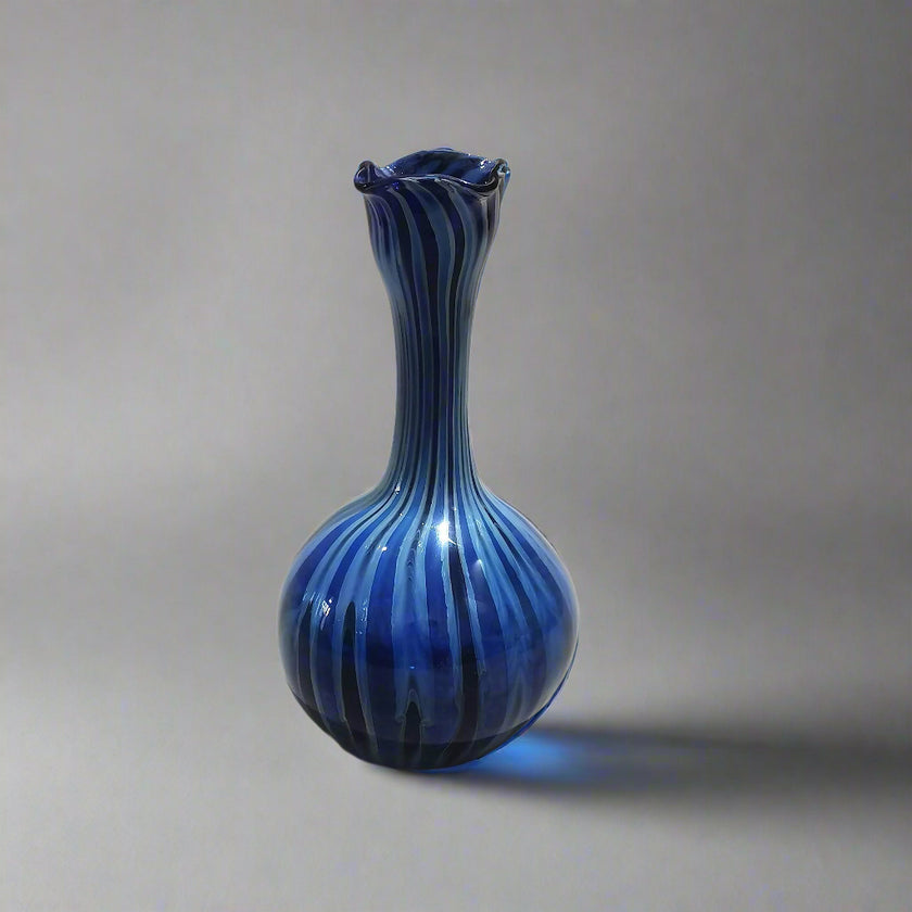 A handblown glass vase with blue hues and swirling patterns, placed against a neutral background.