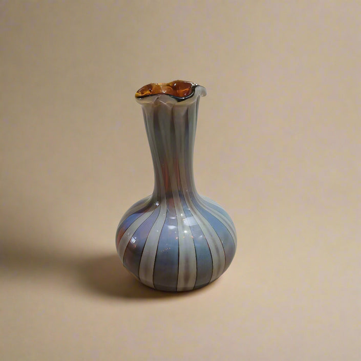 A handblown glass vase with a Murano-style design, featuring earthy hues and vertical stripes, on a neutral background.
