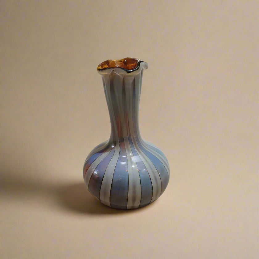 A handblown glass vase with a Murano-style design, featuring earthy hues and vertical stripes, on a neutral background.