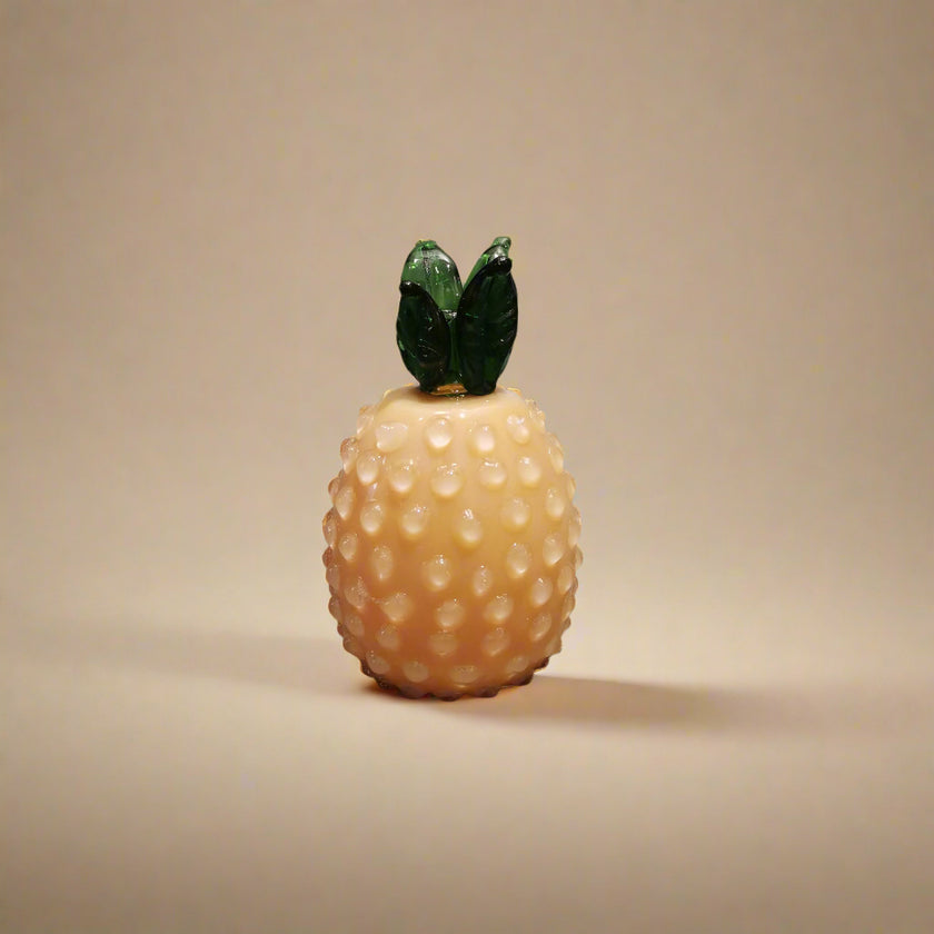 Handblown glass pineapple decoration with a yellow body and green leaves on top.