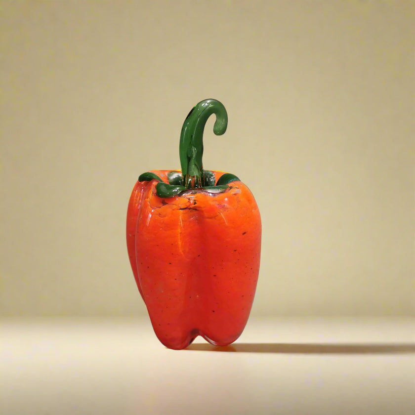 A handblown glass vase in the shape of a red bell pepper with a vibrant red finish and a curved green stem.