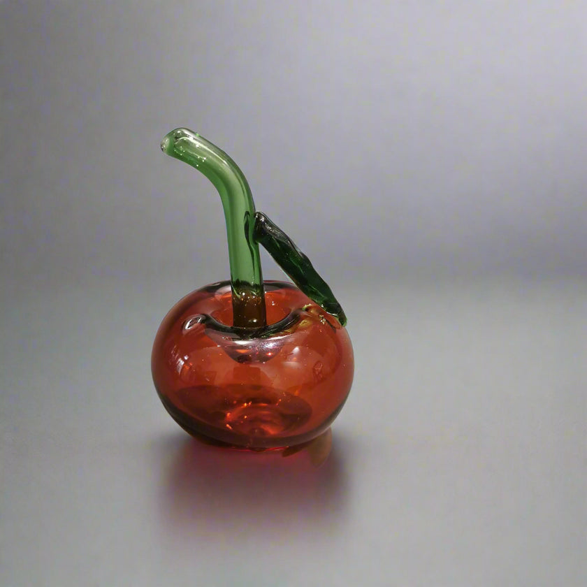 A handblown glass apple-shaped decoration with a green stem and red body.
