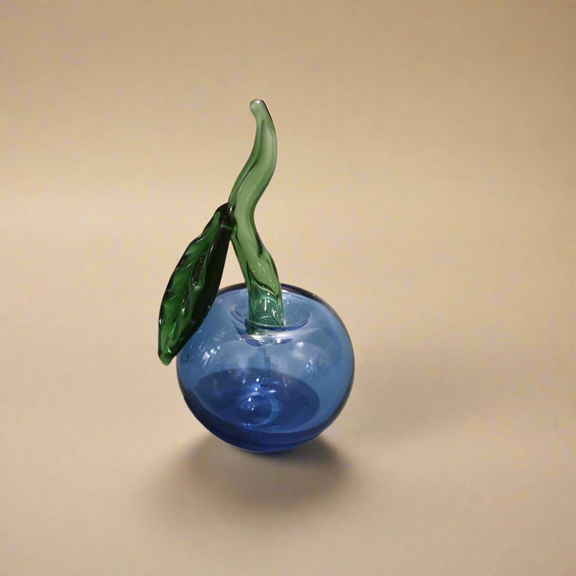 Handblown glass apple decoration with a blue body and green leaf on a grey background