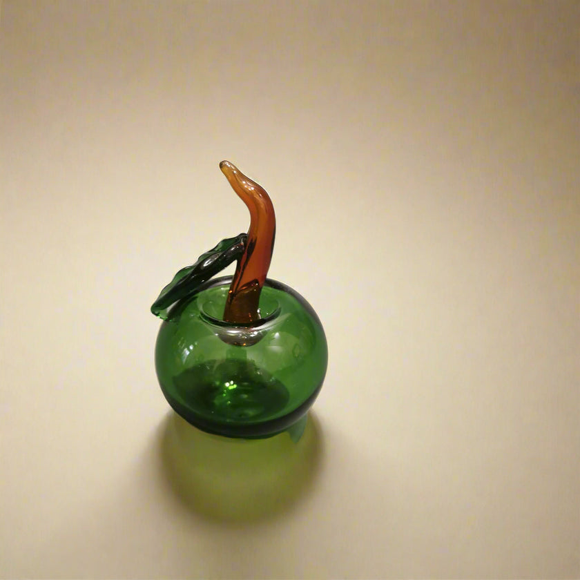 A handblown glass apple decoration with a leaf-like protrusion, featuring a realistic natural color.
