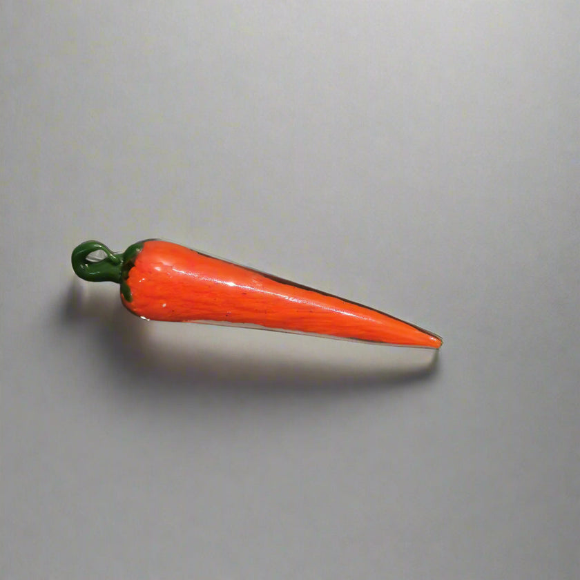Handblown glass chilli decoration with a vibrant orange body and green stem, lying on a grey surface.