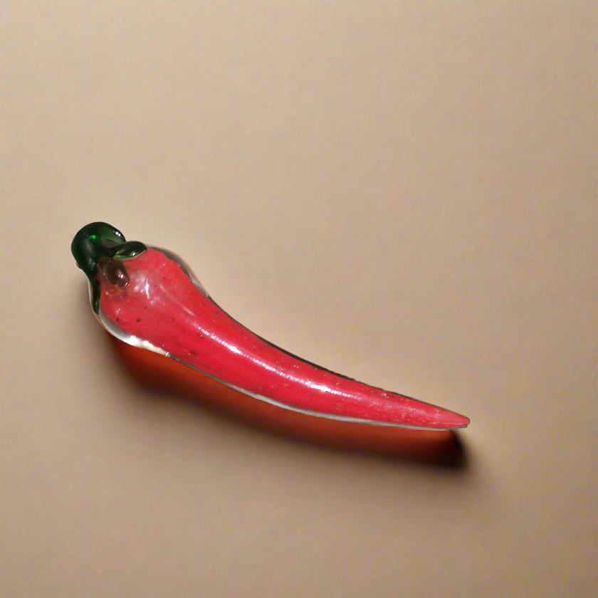 A handblown glass chilli decoration piece with a red color and a green rim at the top.