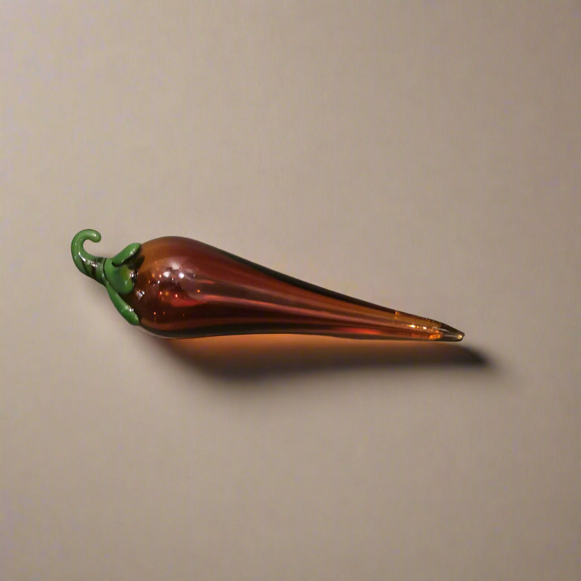 Handblown glass chilli decoration with a dark amber body and green stem.