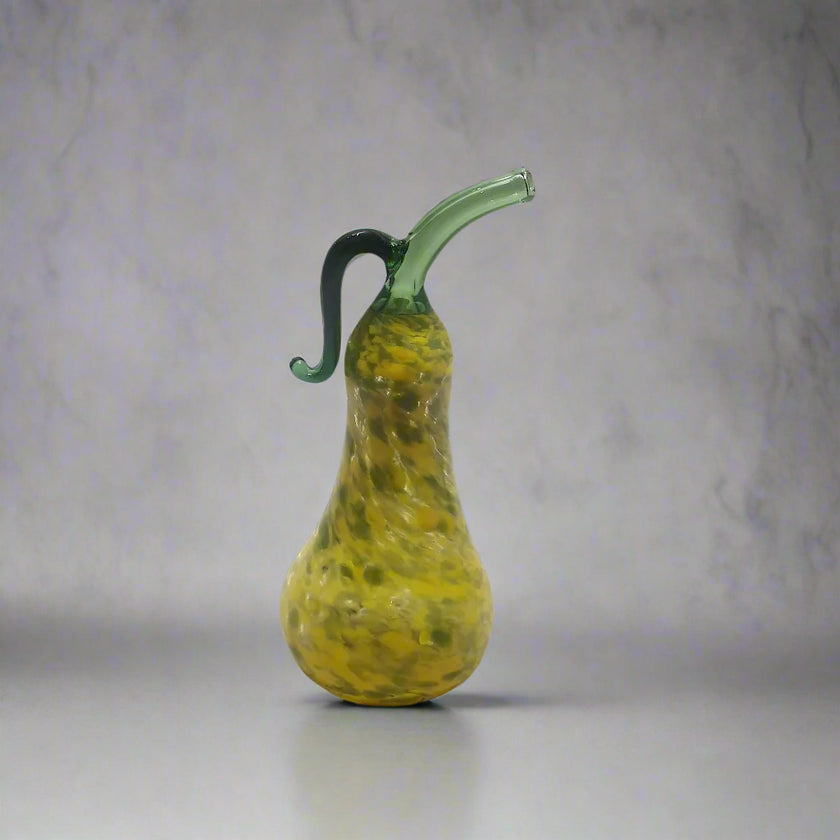 Handblown glass pear-shaped decoration with a green stem and a yellow body, placed on a white surface.