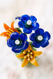 Colorful glass flower brooch with blue and orange flowers on a blurred background