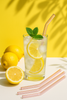 Glass of lemonade with lemon slices and a straw on a yellow background