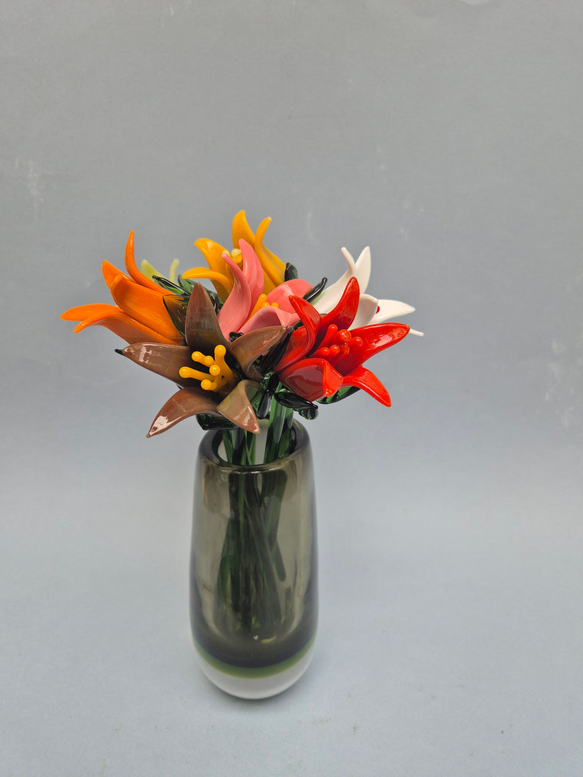 Small glass bottle with colorful artificial flowers on a gray background