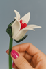 Hand holding a glass flower with white petals and red center against a gray background