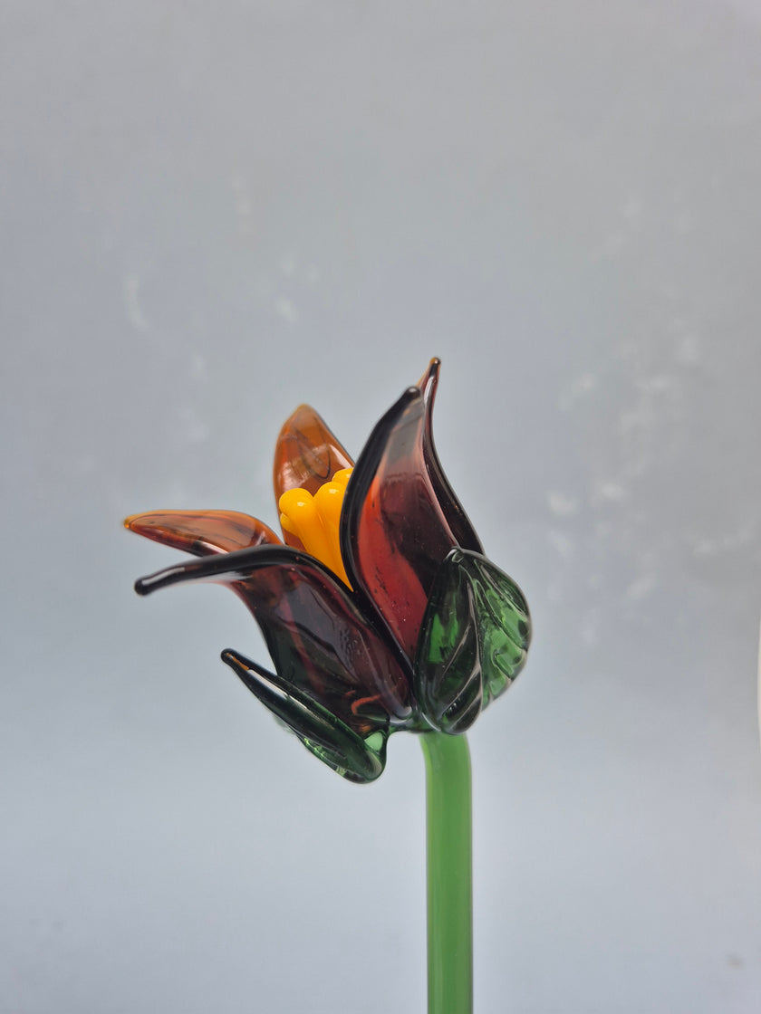 Glass sculpture of a flower with green leaves and yellow center on a gray background
