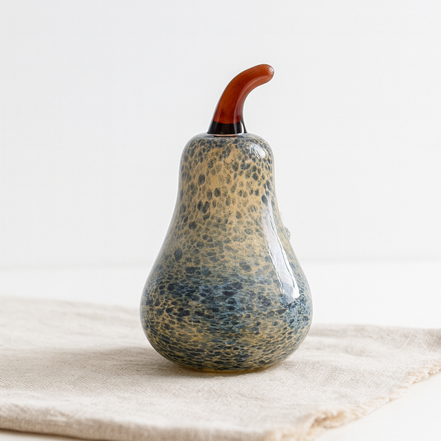 Decorative glass pear with speckled design on a light fabric surface