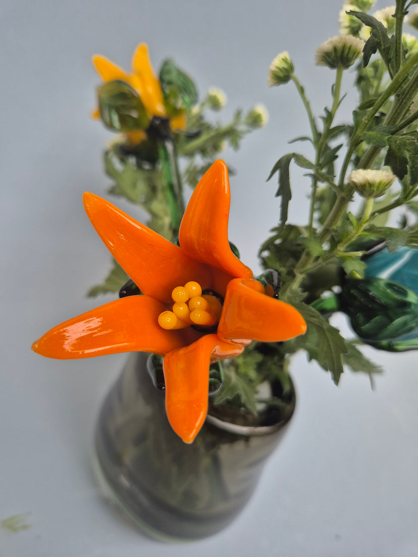 Close-up of an orange artificial flower with green leaves on a light gray background