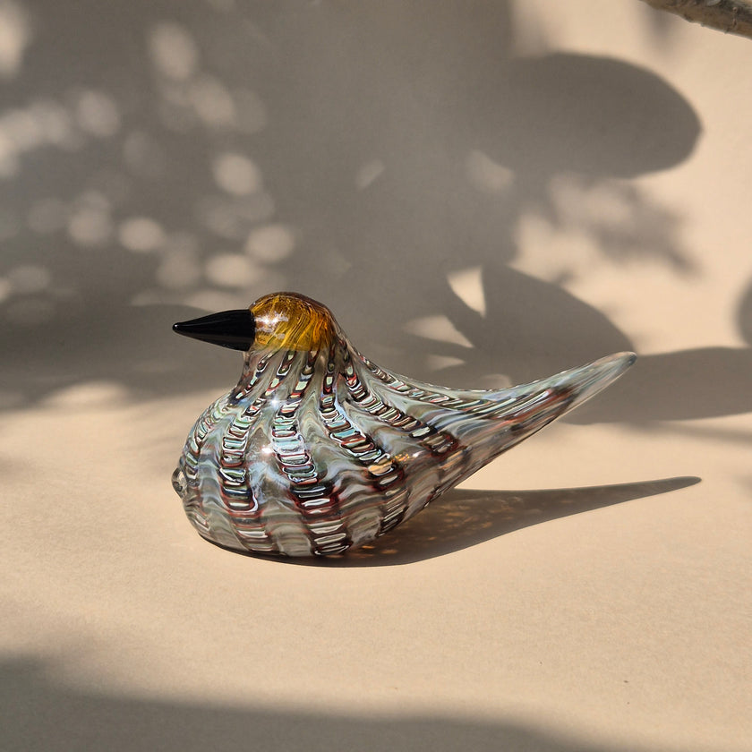 A glass bird figurine with marbled patterns and golden accents, displayed against a shadowed background.