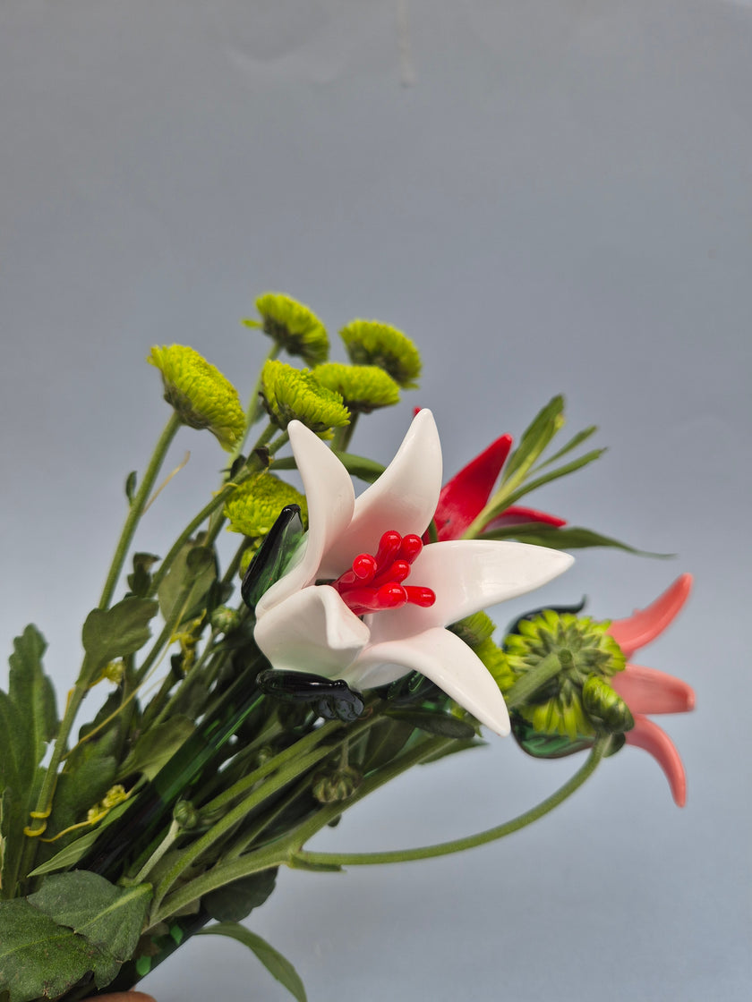 Artificial flower arrangement with green leaves and a white flower with red center on a gray background